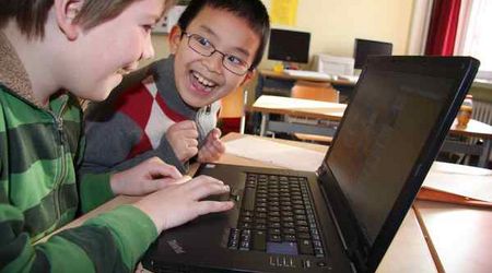 Zwei Jungen sitzen zusammen an einem Laptop und haben Spaß