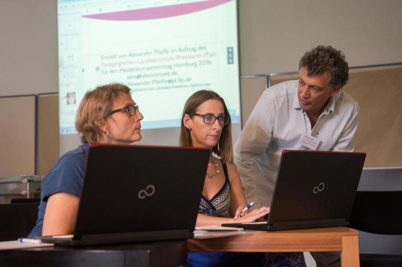 Workshop-Situation: Zwei Frauen am Laptop, ein Mann unterhält sich mit ihnen
