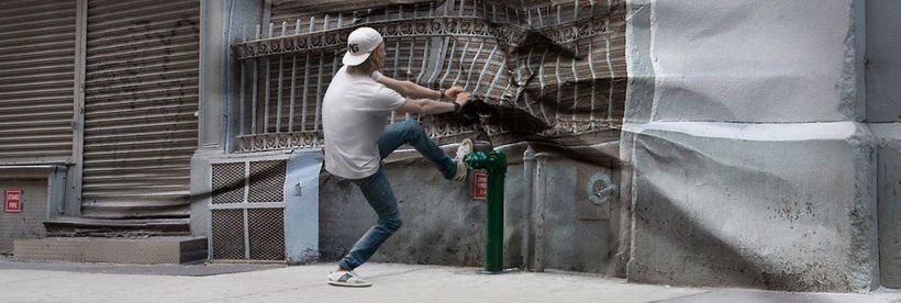 Ein junger Mann zieht an der Hauswand, die Wand verhält sich wie Papier