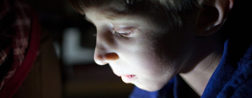 Das Gesicht eines Jungen wird in einem dunklen Raum hell angestrahlt