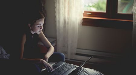 Ein junges Mädchen sitzt auf Ihrem Bett am Laptop