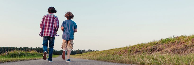 Ansicht von hinten, wie zwei Jungen eine Straße entlang laufen
