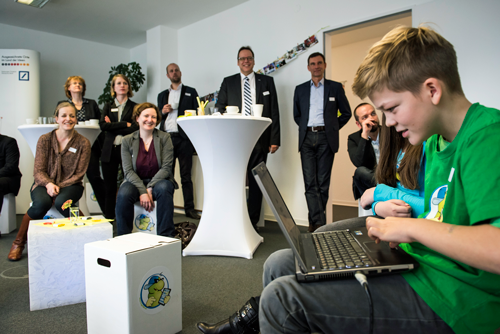 Ein Junge sitzt an einem Laptop, einige Menschen schauen im zu
